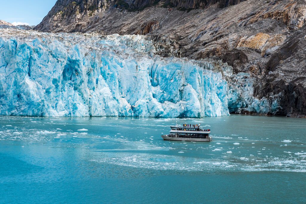 Close up view of tourist boat next to glacier face with icy ocean waters