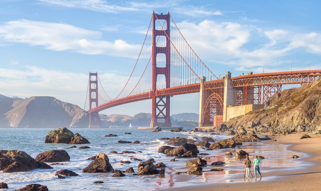 Classic panoramic view of famous Golden Gate Bridge seen from scenic Baker Beach in beautiful golden evening light on a sunny day with blue sky and clouds in summer, San Francisco, California, USA