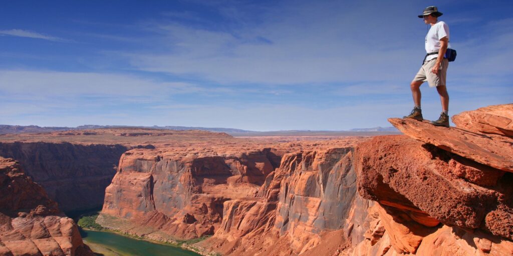 een wandelaar die uitkijkt over Horseshoe Bend, een hoefijzervormige meander van de Colorado River nabij de stad Page in Arizona.