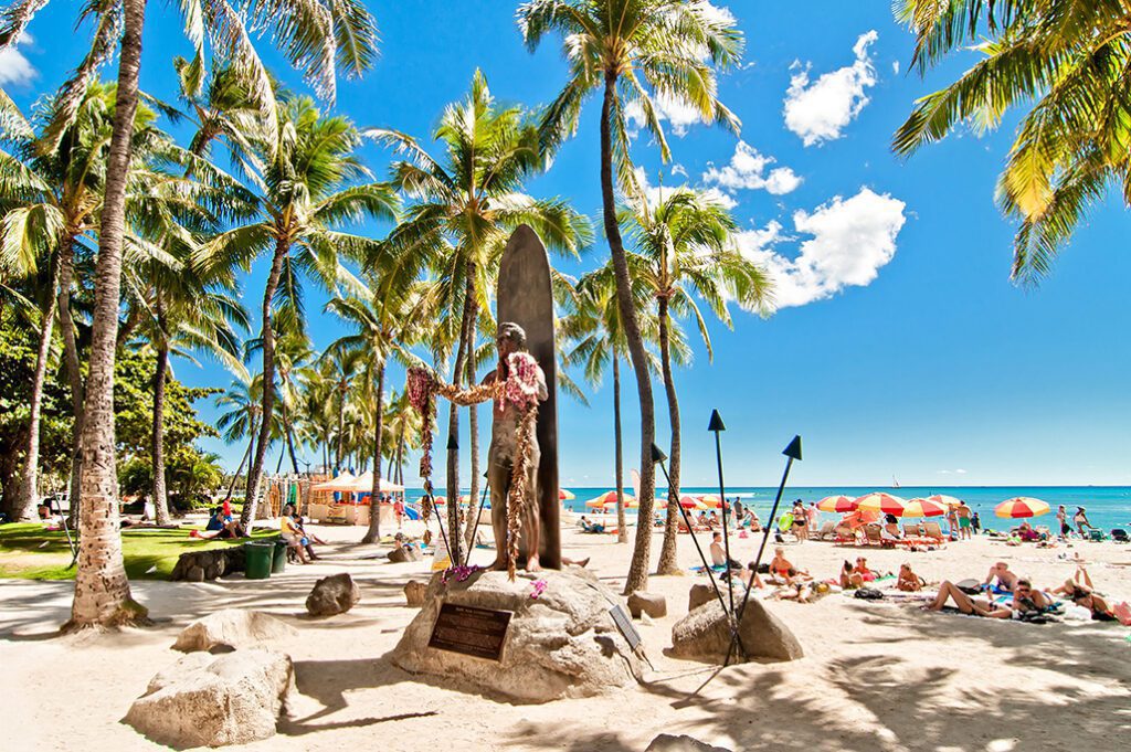 Tourists sunbathing and surfing on Waikiki beach in Honolulu, Hawaii. Waikiki white sand beach shoreline is Hawaii's most famous beach.