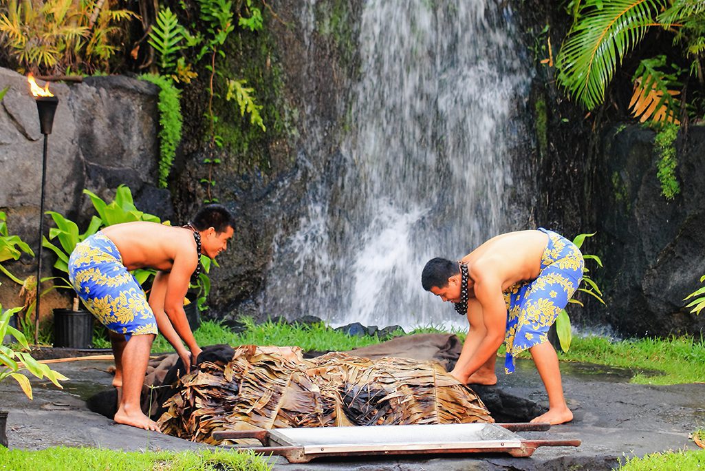 Two young Hawaiian men at the Polynesian Cultural Center uplift a pig cooked in the traditional style Kalua utilizing an Imu (under ground oven)