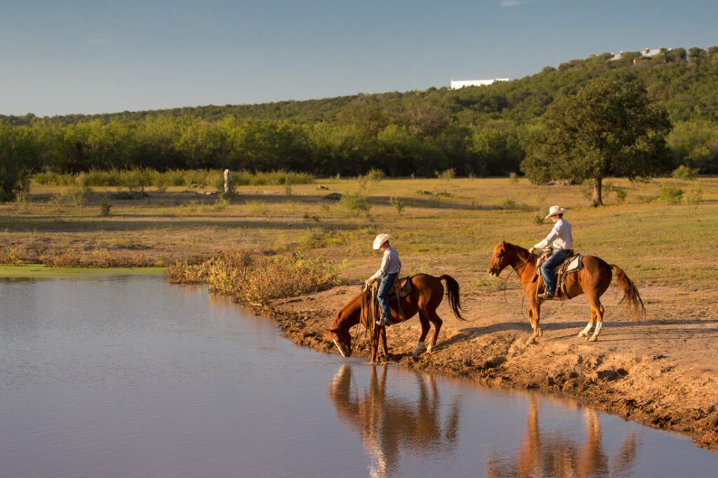 twee ruiters in een veld, een paard gaat drinken van een vijver
